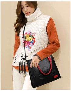 Detail of black embossed leather tote with red handles and floral patterns