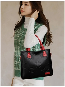 Detail of embossed floral patterns and red handles on a black leather tote bag