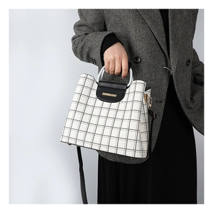 Detail of checkered crossbody bag showing metal handle, flap closure and leather strap