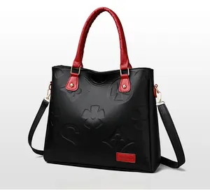 Detail of embossed clover pattern on black lychee leather handbag with red handles
