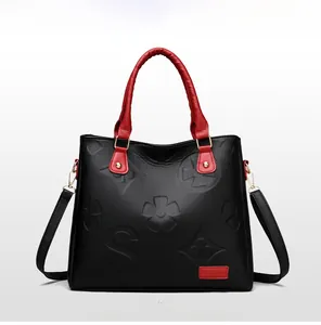 Close-up of black embossed floral leather handbag with red straps and gold hardware