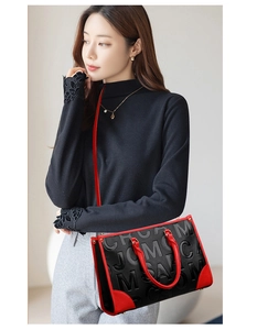 Détail d'un sac cabas noir et rouge avec lettres embossées et poignées rouges