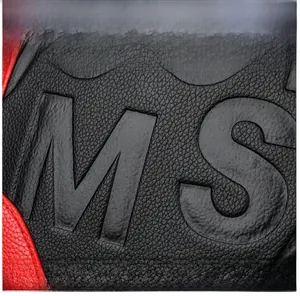 Détail macro du sac en cuir grainé noir avec motif MS embossé et bordures rouges