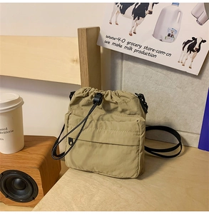 Khaki nylon drawstring crossbody bag with hidden zipper pocket on a wooden tabletop
