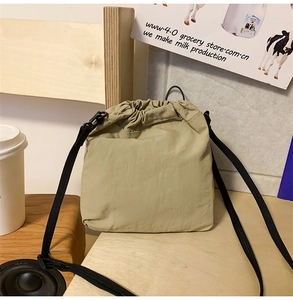Detailed view of khaki drawstring crossbody bag on wooden table with lifestyle props