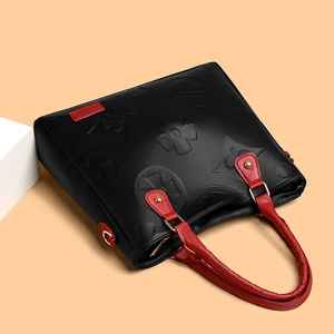 Black embossed leather tote bag with red handles and large floral pattern details