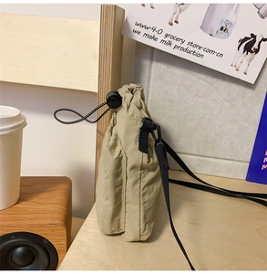 Detail of khaki drawstring crossbody bag with black cord strap and toggle on wooden table