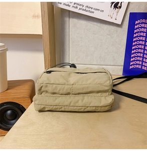 Detail of khaki nylon pleated crossbody bag with double zippers on a wooden table