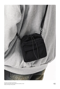 Detail of a black nylon crossbody phone bag with drawstring and front zipper pocket