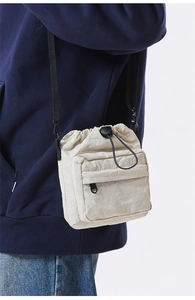 Side view of cream drawstring crossbody bag in lightweight nylon worn over blue hoodie