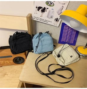 Three pleated nylon drawstring mini crossbody bags in black, sky blue and off-white colors
