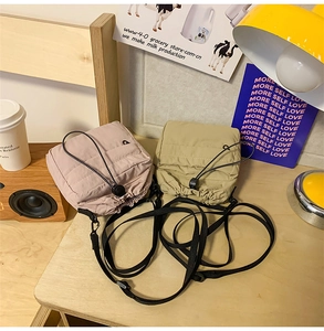 Nylon drawstring crossbody phone bags in pink and beige on a wooden desk with a lamp