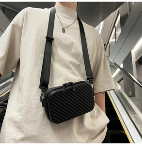 Close-up of a black hard-shell crossbody bag with groove texture and nylon shoulder strap