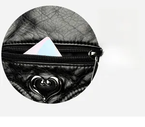 Detail of black textured leather bag with heart-shaped metal buckle and zip pocket