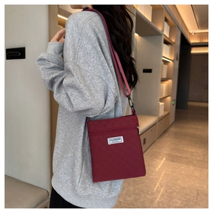 Détail du sac bandoulière en nylon matelassé bordeaux avec écusson sur le mannequin