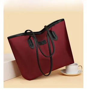 Dettaglio della borsa tote in nylon bordeaux con manici in pelle nera e logo applicato