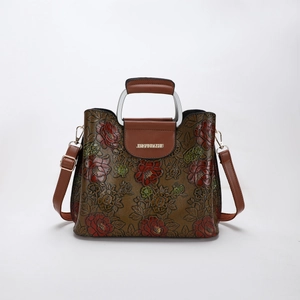 Detailed view of 3D embossed floral patterns and sturdy metal handle on brown handbag