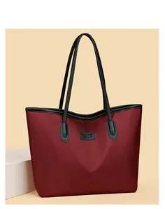 Dettaglio della borsa tote in nylon bordeaux con manici in pelle nera e logo
