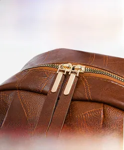 Close-up of premium gold-tone dual zippers on textured brown leather backpack