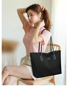 Dettaglio di una grande borsa tote nera con manici lunghi indossata da una modella