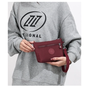 Detail einer weinroten Nylon-Mini-Tasche mit rundem Logo und vorderem Reißverschluss