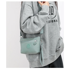 Detail der hellgrünen Nylon-Umhängetasche mit Logo und vorderer Reißverschlusstasche