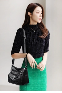 Detail of black multi-zipper crossbody bag with heart rivets and soft pebble texture