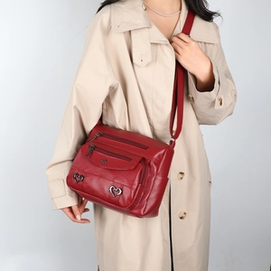 Detail of red leather crossbody bag with multiple zip pockets and heart metal buckles