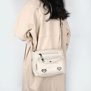 Close-up of multi-pocket crossbody bag with heart charms and zippers on cream leather