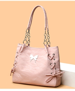 Detail of pink leather tote bag featuring bow accents and silver butterfly ornament