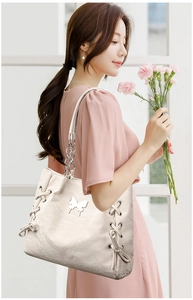 Detail of cream tote bag featuring silver butterfly buckle and lace-up side design