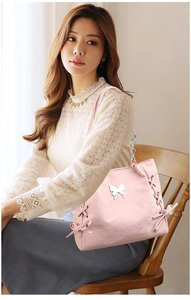 Detail of pink PU leather tote featuring side bow ties and silver butterfly charm pendant