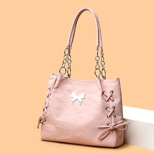 Pink pleated leather tote bag with silver butterfly charm and chain straps on orange background