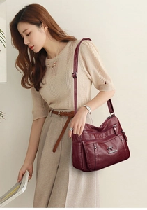 Detail of burgundy PU leather shoulder bag with multiple zippers and adjustable strap