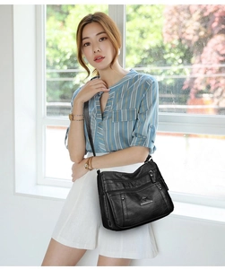 Detail of black faux leather crossbody bag with multiple zippers and gold logo on a model