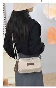 Rear view of a beige oxford crossbody bag worn by a model in a minimalist setting