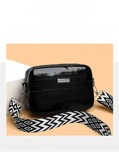Detail of black glossy crossbody bag with textured wave pattern and woven wide strap