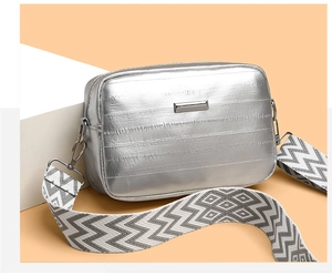 Detailed close-up of metallic silver crossbody bag with woven wide shoulder strap