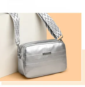 Detail of silver metallic crossbody bag with quilted texture and wide patterned strap