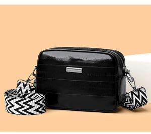 Macro view of black patent leather crossbody bag with silver hardware and woven strap