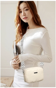 Macro detail of creamy crossbody bag showing geometric textured wide strap and metal trim