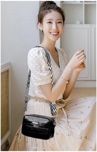 Detail of black crossbody bag with silver hardware and patterned wide textile strap