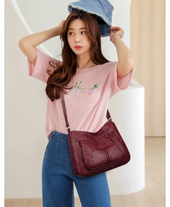 Detail of wine red faux leather crossbody bag with multiple zip pockets on model