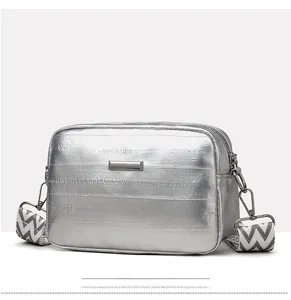 Close-up of silver textured crossbody bag with patterned wide strap and metallic buckle