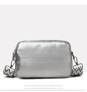 Silver metallic crossbody bag showing wide woven shoulder strap and rear stitching details