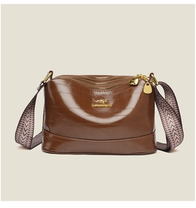 Detail of dark brown crossbody bag with three zipper compartments and patterned strap