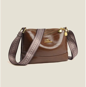 Detail of brown leather crossbody bag featuring triple gold zippers and woven shoulder strap