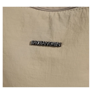 Detailed close-up of beige nylon bucket bag featuring a black BAOJIANGREN metal logo plate