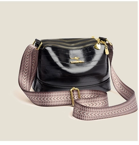 Detailed view of black patent leather crossbody bag with triple gold zippers and woven strap