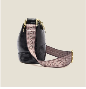 Detail of black glossy handbag with adjustable patterned strap and golden hardware